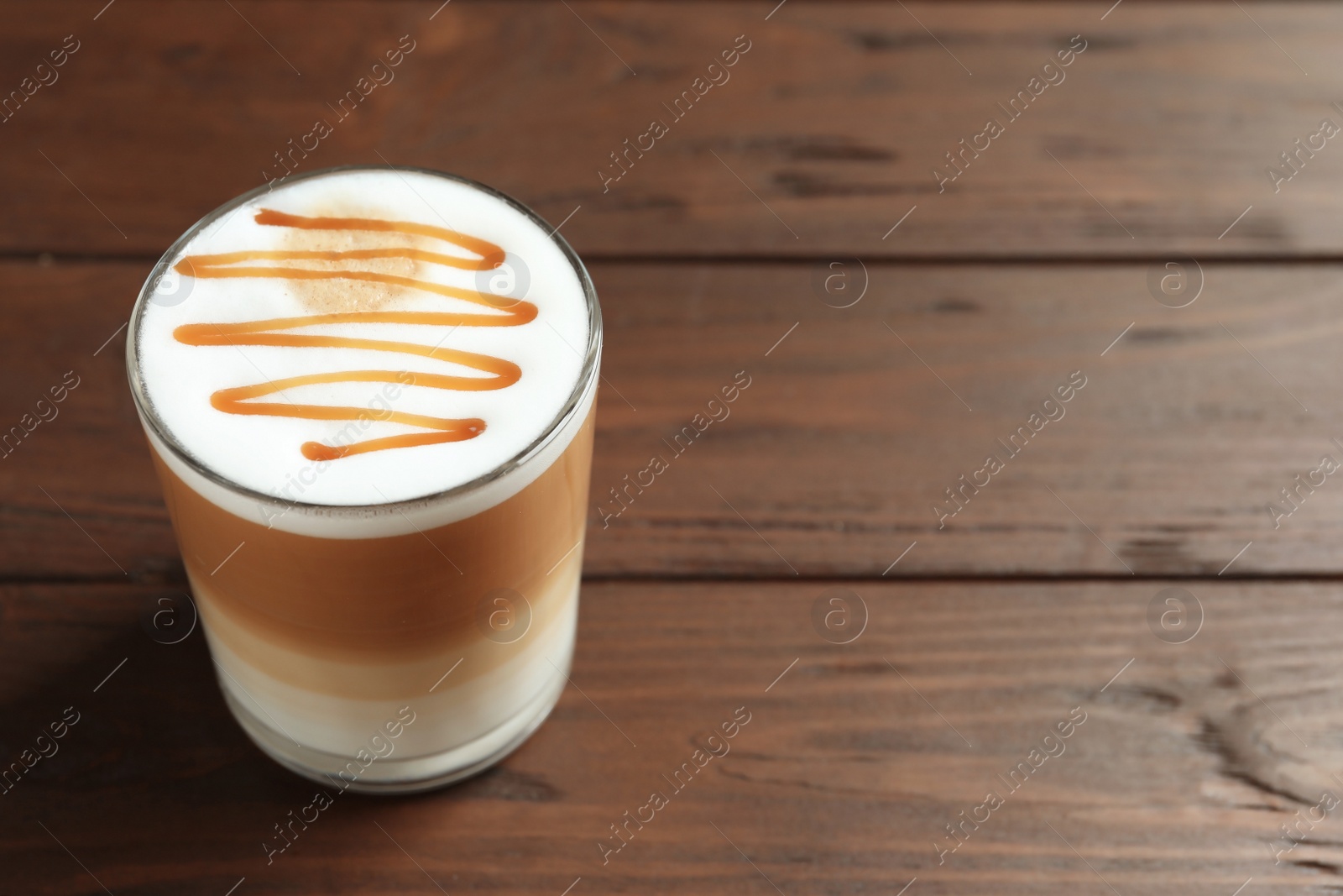 Photo of Glass with delicious caramel latte on wooden background