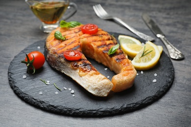 Photo of Slate plate with tasty salmon steak on grey background