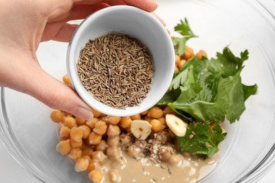 Photo of Woman adding cumin into bowl with ingredients for delicious hummus, closeup