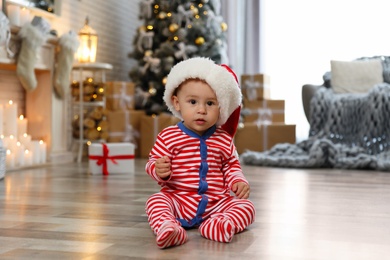 Photo of Little baby wearing Santa hat on floor at home. First Christmas