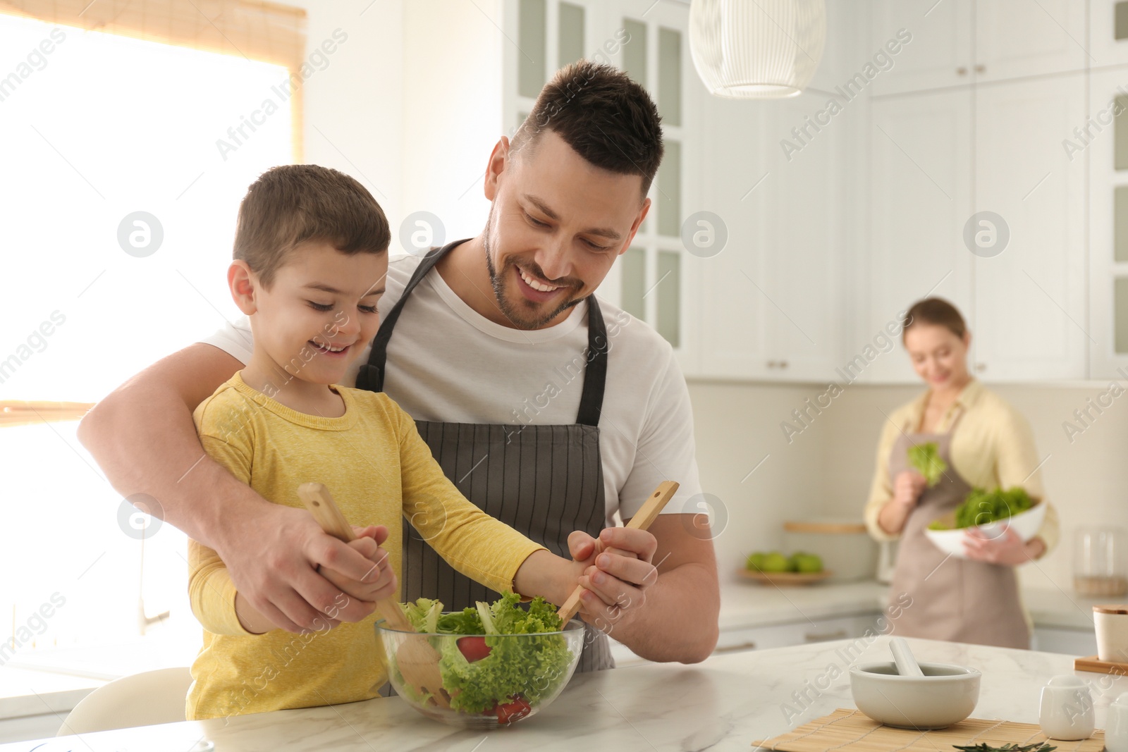 Photo of Happy family cooking salad together in kitchen