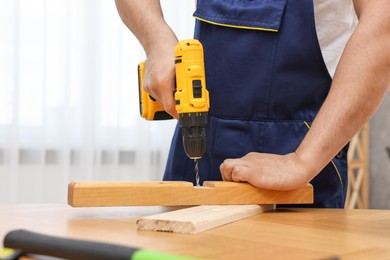 Young worker using electric drill at table in workshop, closeup