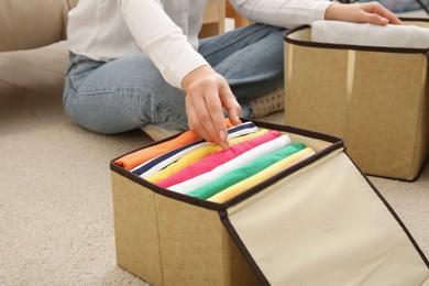 Photo of Woman folding clothes on floor at home, closeup. Japanese storage system