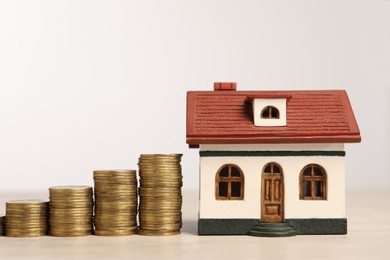 Photo of Mortgage concept. House model and stacks of coins on wooden table against white background