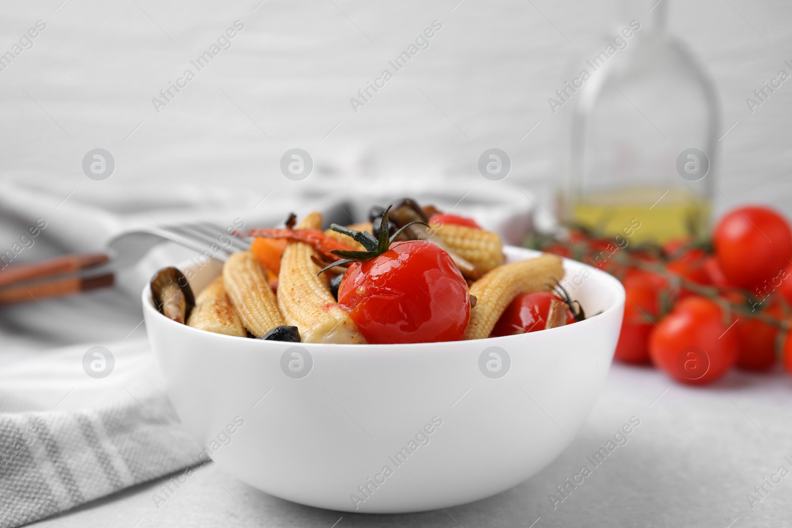 Photo of Tasty roasted baby corn with tomatoes on light grey table, closeup