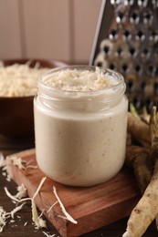 Photo of Spicy horseradish sauce in jar on wooden table, closeup
