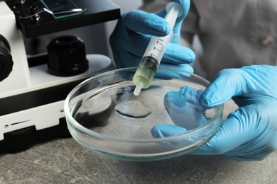 Doctor dripping urine from syringe into petri dish at grey table, closeup