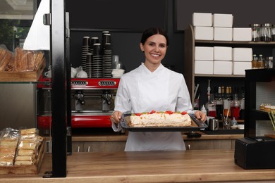 Photo of Happy baker presenting delicious cake with strawberries in cafe
