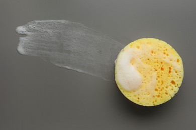 Yellow sponge with foam on grey background, top view