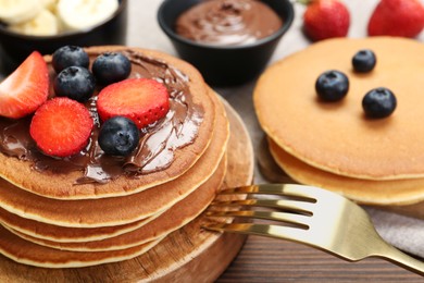 Photo of Tasty pancakes with chocolate paste, berries and fork on wooden table, closeup