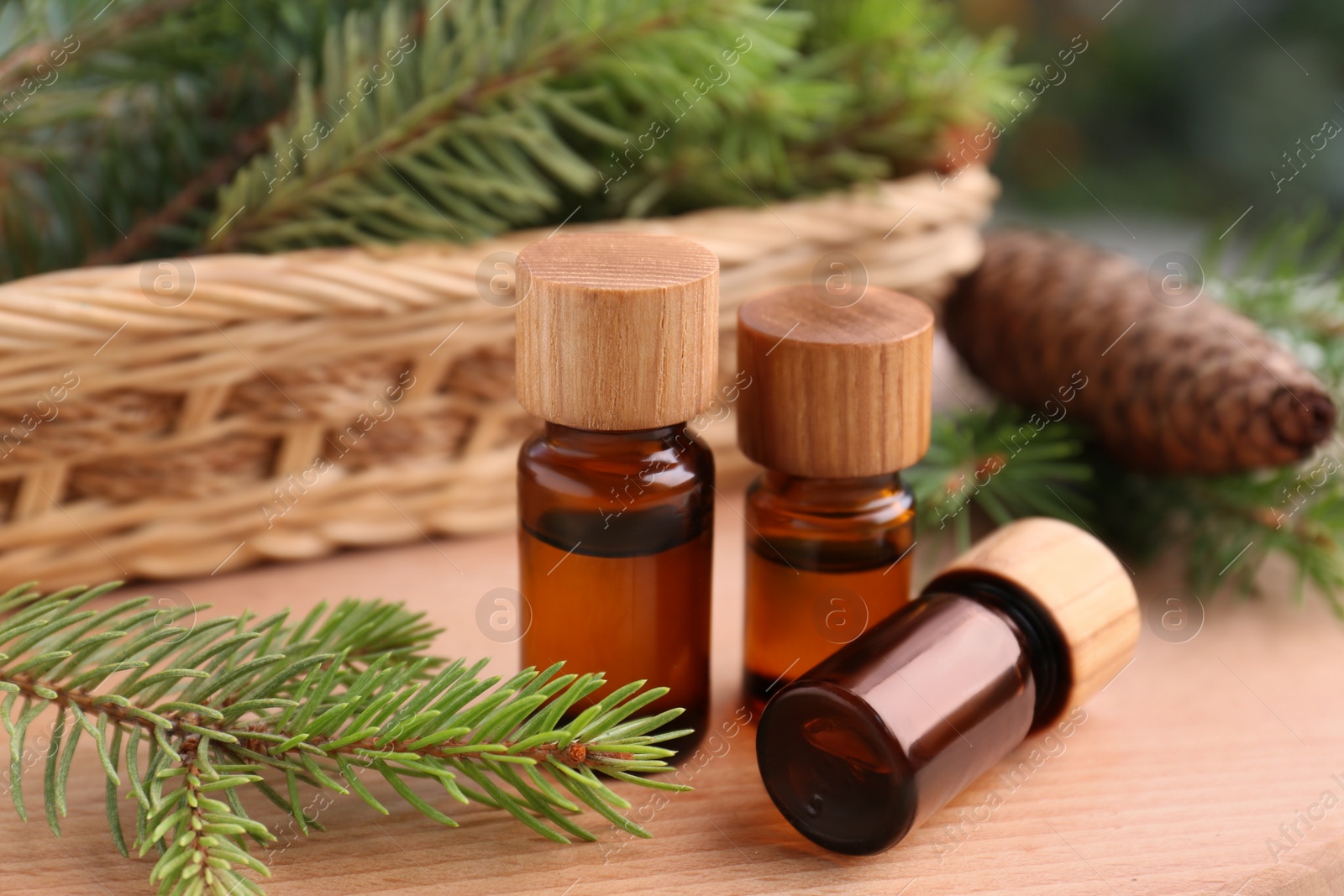 Photo of Bottles of pine essential oil, cone and branches on wooden table, closeup