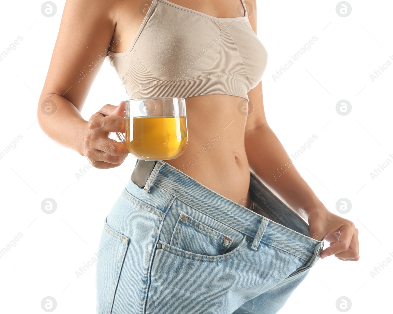 Photo of Young woman in old big jeans with cup of tea showing her diet results on white background, closeup