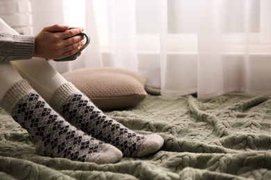 Photo of Woman relaxing with cup of hot winter drink on knitted plaid at home, closeup. Space for text