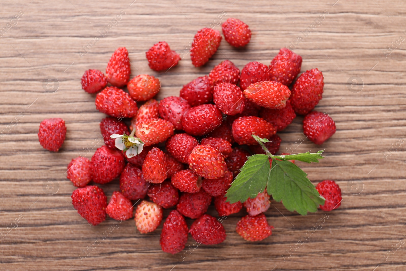 Photo of Pile of wild strawberries, flower and leaves on wooden table, flat lay