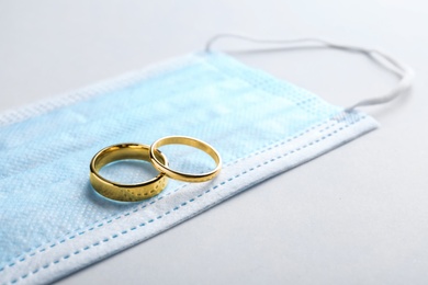 Photo of Wedding rings and medical mask on grey background, space for text. Divorce during coronavirus outbreak