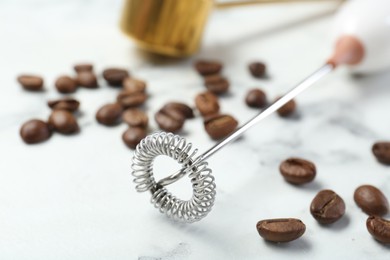 Photo of Milk frother wand and coffee beans on white marble table, closeup