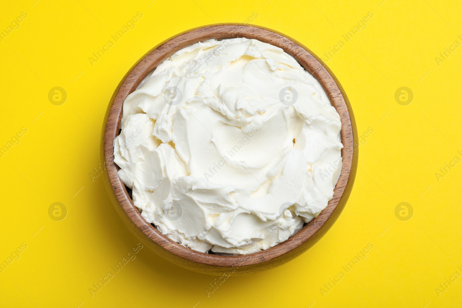 Photo of Bowl of tasty cream cheese on yellow background, top view