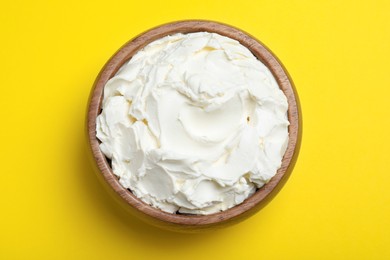 Photo of Bowl of tasty cream cheese on yellow background, top view