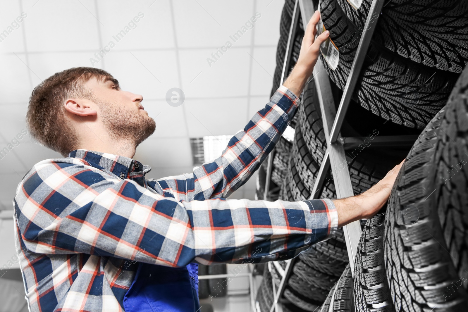 Photo of Young male mechanic with car tires in automobile service center