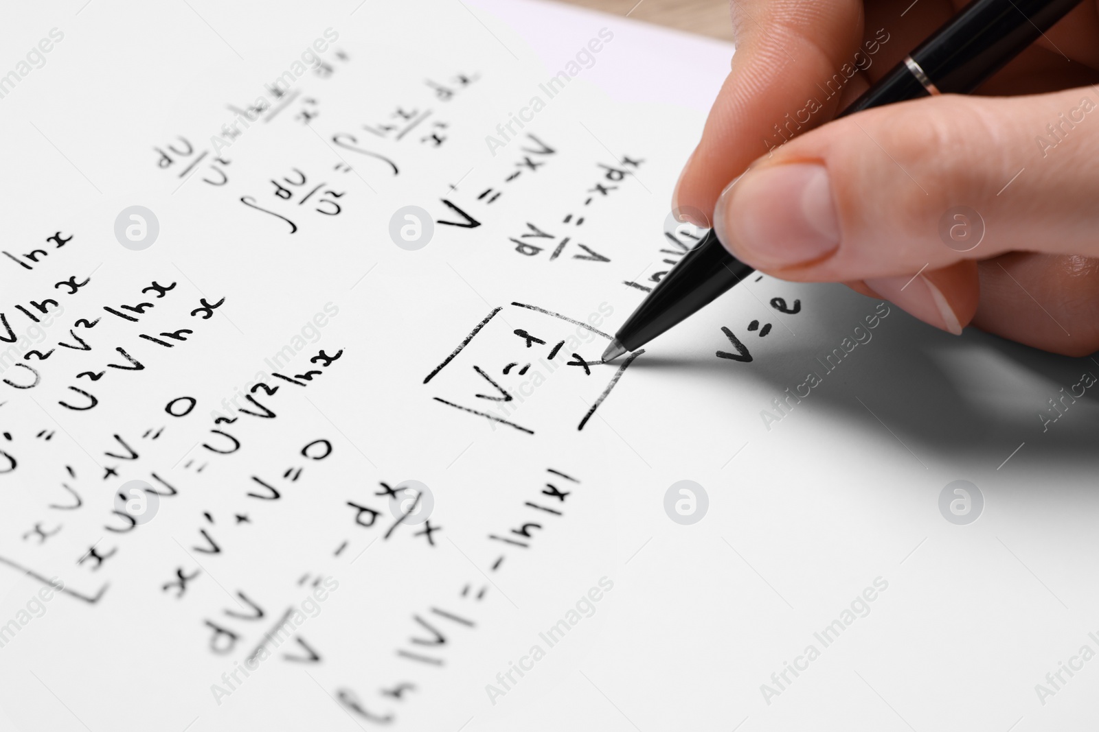 Photo of Student writing different mathematical formulas on paper, closeup