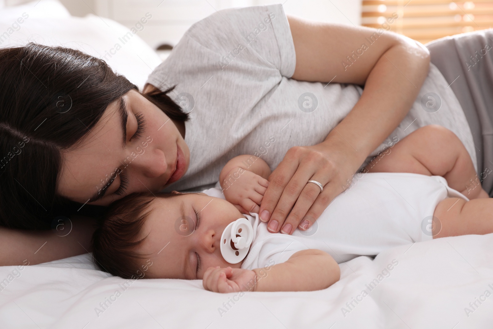 Photo of Young mother resting near her sleeping baby on bed at home