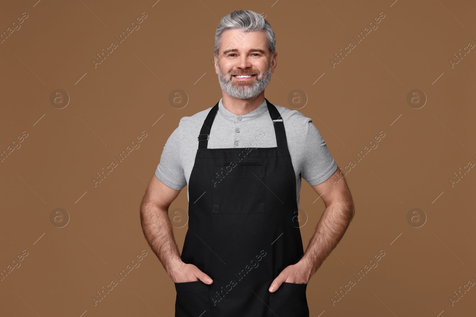 Photo of Happy man wearing kitchen apron on brown background. Mockup for design