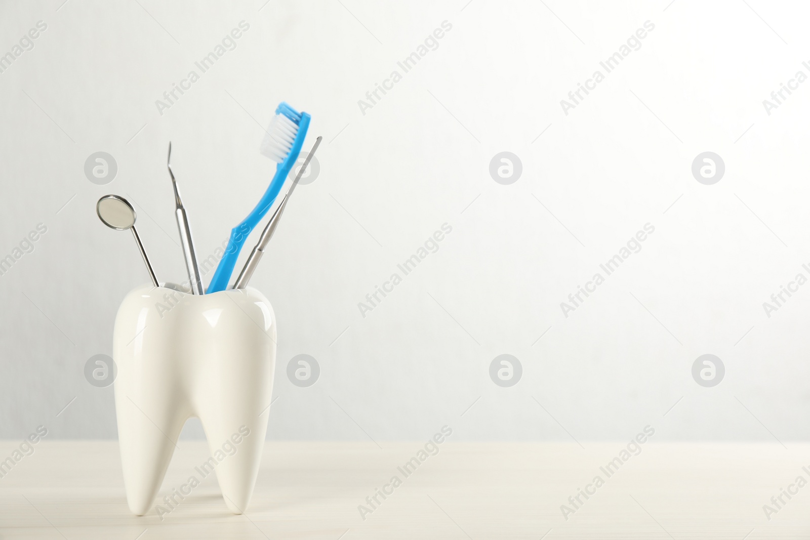 Photo of Tooth shaped holder with set of dentist's tools and brush on wooden table. Space for text