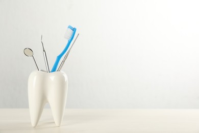 Photo of Tooth shaped holder with set of dentist's tools and brush on wooden table. Space for text