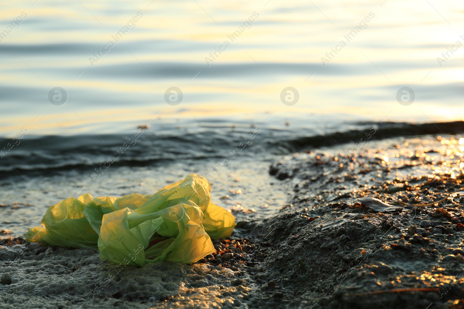 Photo of Used plastic bag near water at beach, space for text. Environment pollution