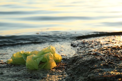 Photo of Used plastic bag near water at beach, space for text. Environment pollution