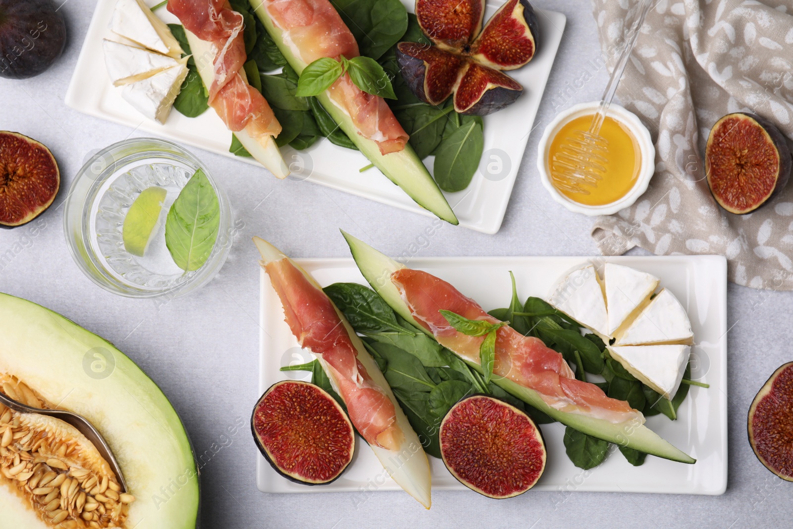 Photo of Tasty melon, jamon and figs served on light grey table, flat lay