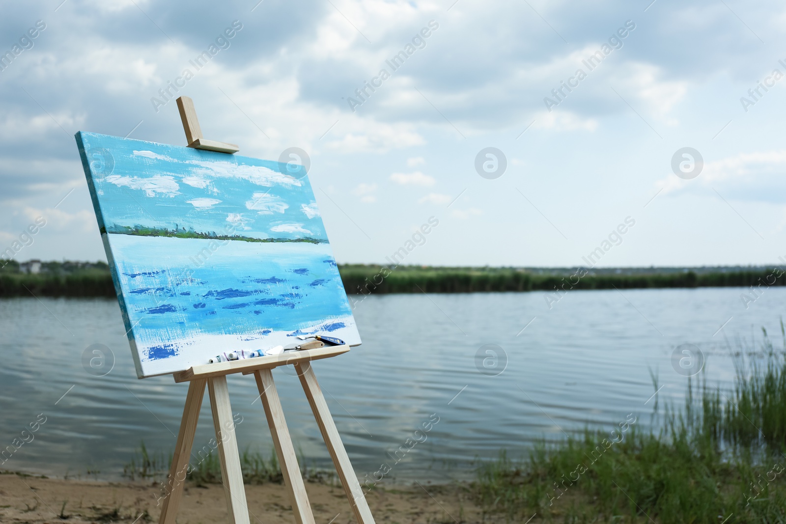 Photo of Wooden easel with unfinished painting near lake