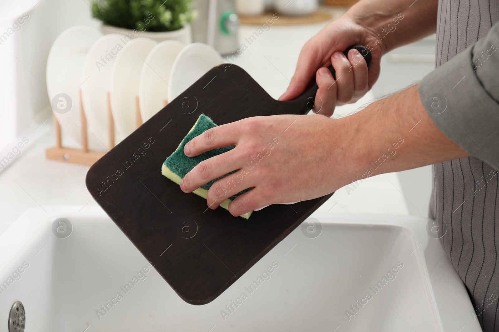 Photo of Man washing dark wooden cutting board at sink in kitchen, closeup