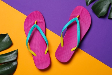 Photo of Bright flip flops and green leaves on color background, flat lay