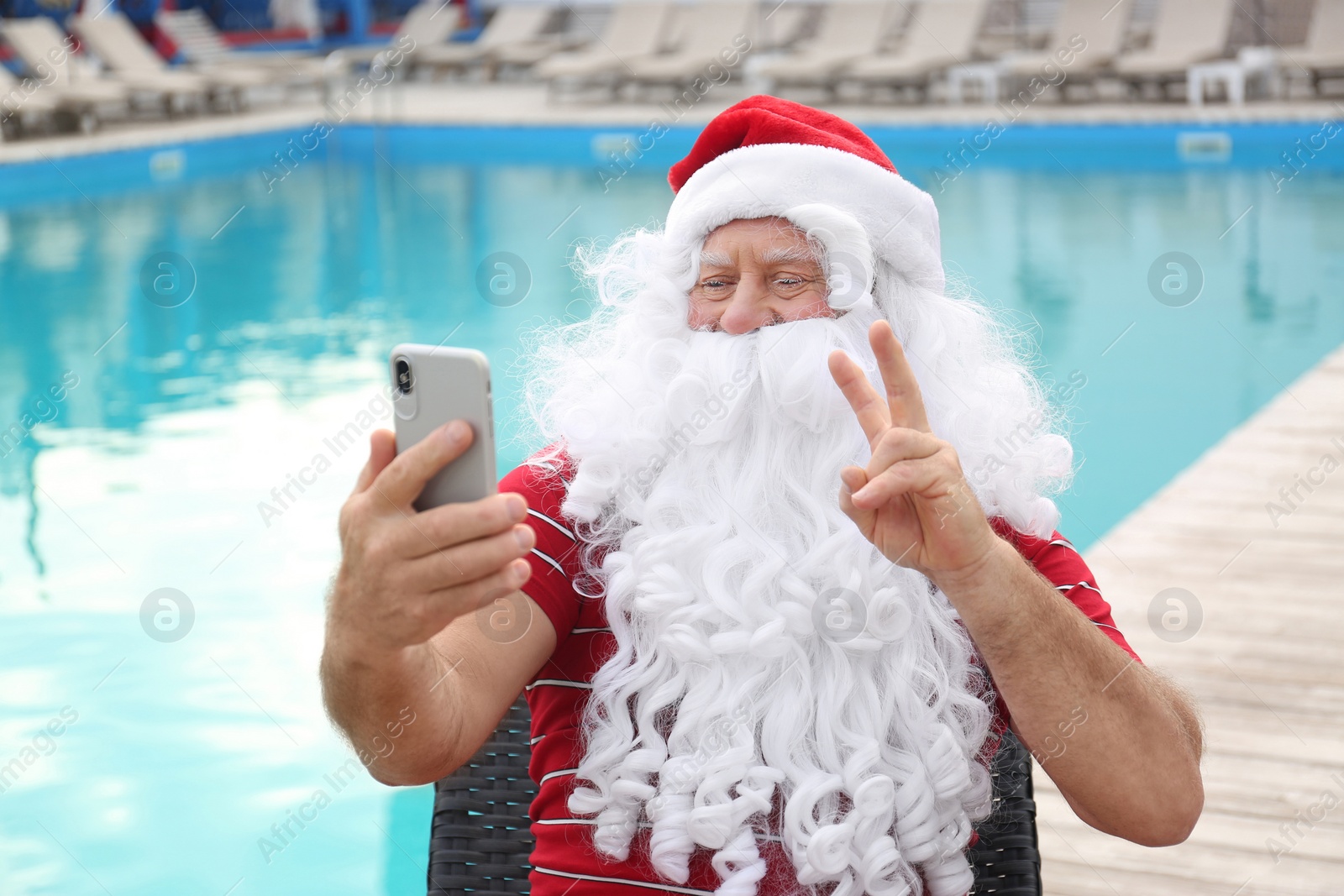 Photo of Authentic Santa Claus taking selfie near swimming pool outdoors