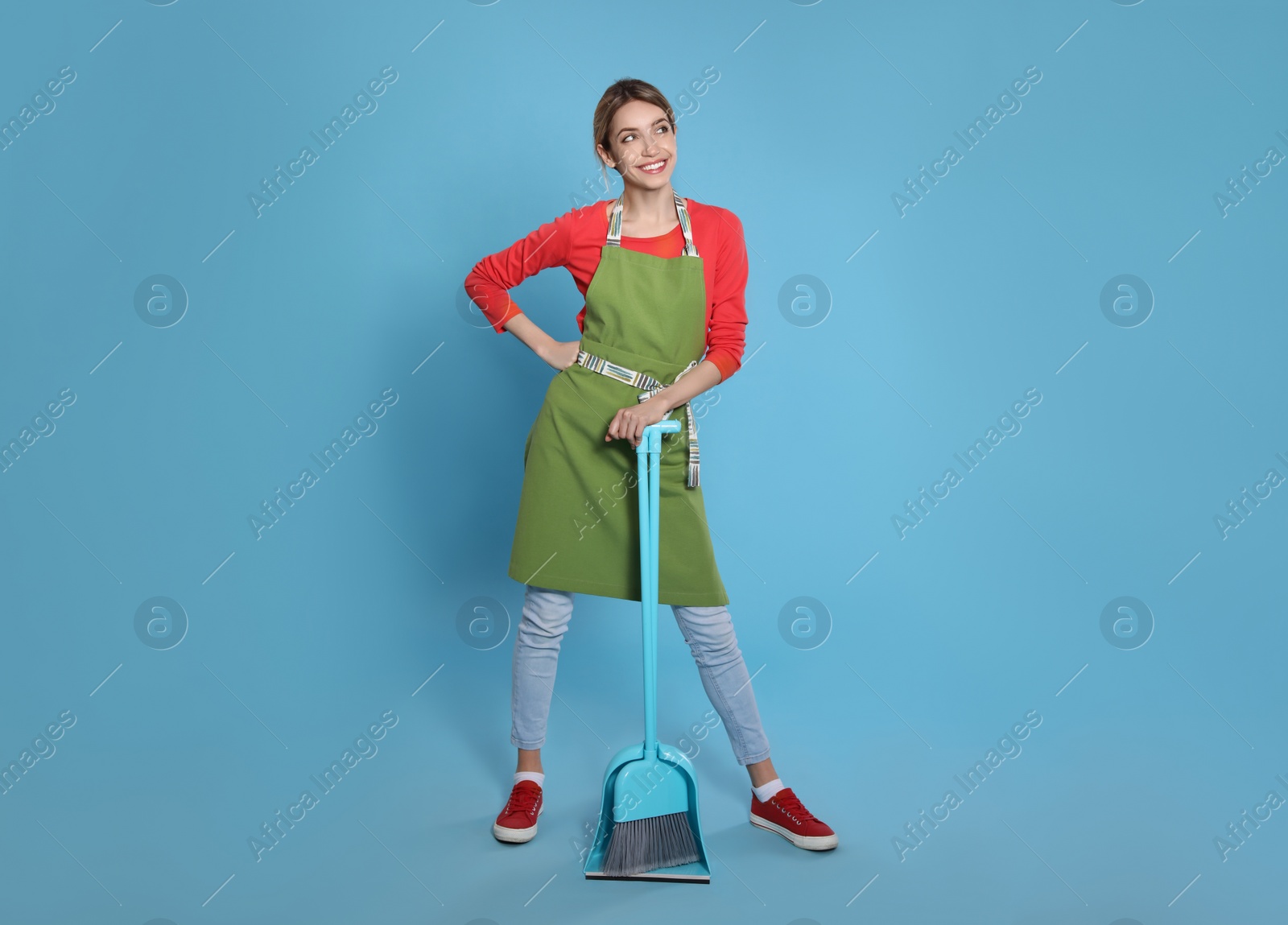 Photo of Young housewife with broom and dustpan on light blue background