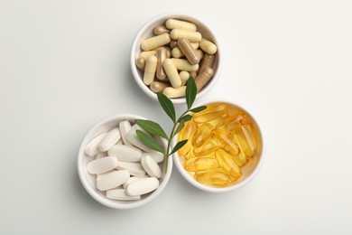 Different vitamin capsules in bowls and leaves on white background, flat lay