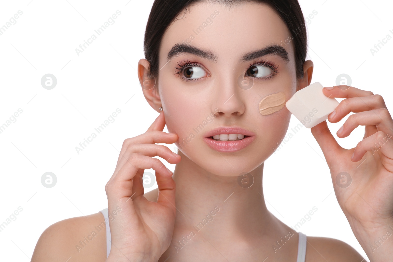 Photo of Teenage girl applying foundation on face with makeup sponge against white background