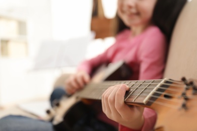 Photo of Little girl playing guitar at home, closeup. Learning music notes