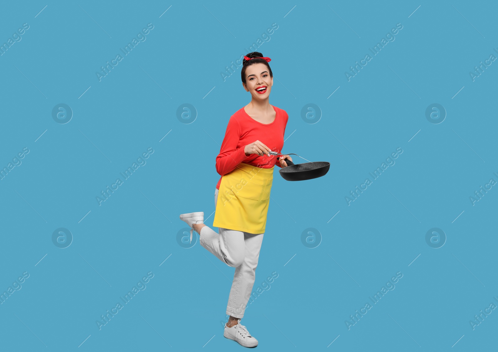 Photo of Housewife with frying pan and spatula on light blue background