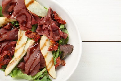 Delicious bresaola salad with sun-dried tomatoes, pear and balsamic vinegar in bowl on white wooden table, top view