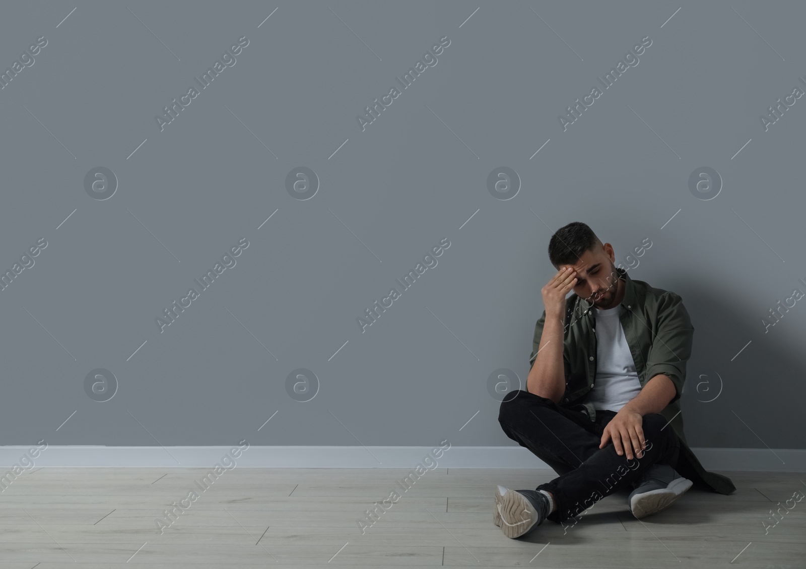 Photo of Sad man sitting on floor near light grey wall. Space for text