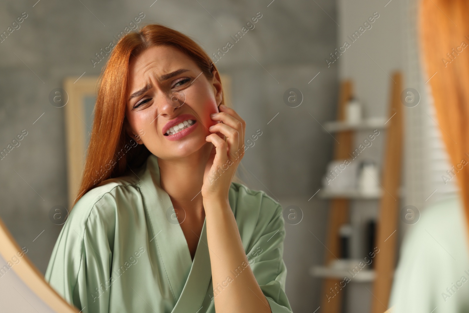 Photo of Suffering from allergy. Young woman checking her face near mirror in bathroom