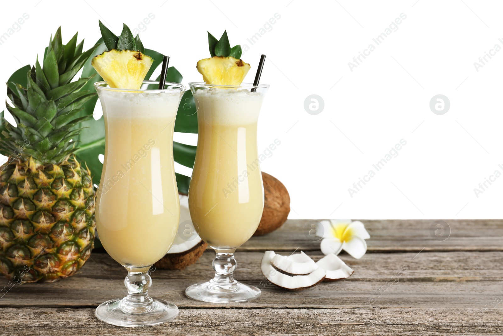Photo of Tasty Pina Colada cocktail and ingredients on wooden table against white background, space for text