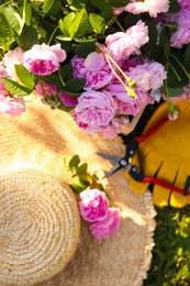 Photo of Top view of straw hat, pruner, gloves and beautiful tea roses outdoors, focus on flowers