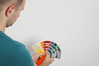 Man with palette choosing color for painting wall indoors, closeup. Interior design