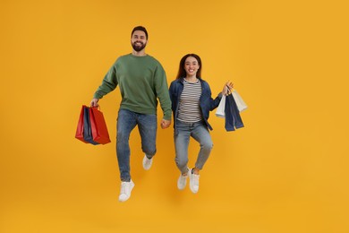 Photo of Happy couple with shopping bags jumping on orange background