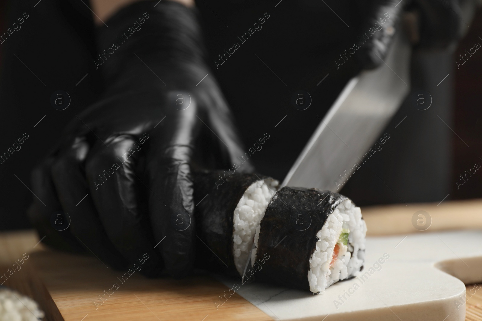 Photo of Chef in gloves cutting sushi roll at table, closeup
