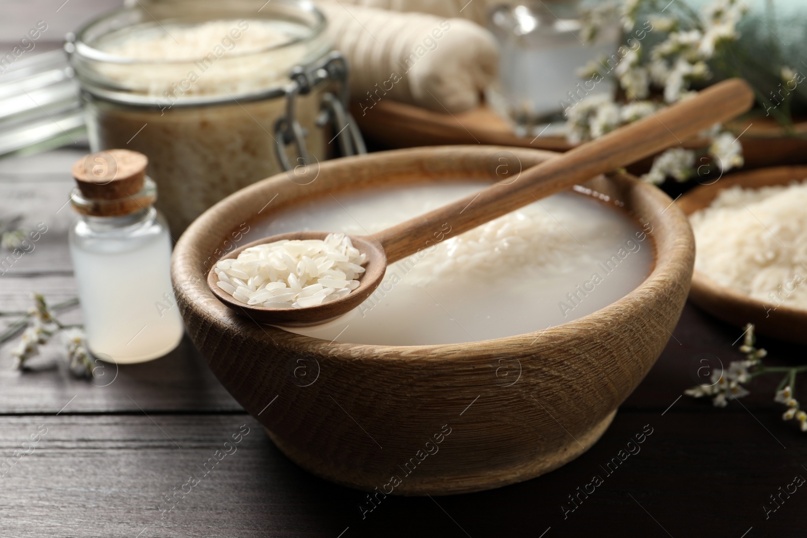 Photo of Bowl with soaked rice and spoon on wooden table, closeup