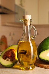 Photo of Fresh avocados and jug of cooking oil on beige marble table in kitchen